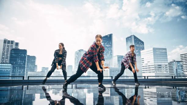 istock Diverse Group of Three Professional Dancers Performing a Hip Hop Dance Routine in Front of a Big Digital Led Wall Screen with Modern Urban Skyline with Skyscrapers in Studio Environment. 1388326426