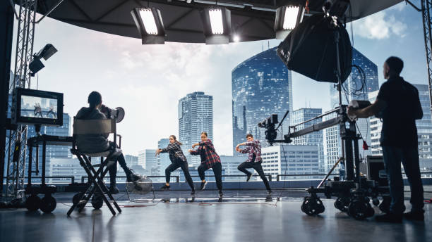 istock Music Clip Studio Set: Shooting Hip Hop Video Dance Scene with Three Professionals Dancers Performing on Stage with Big Led Screen with Modern City Background. Director and Cameraman in Backstage. 1388326464