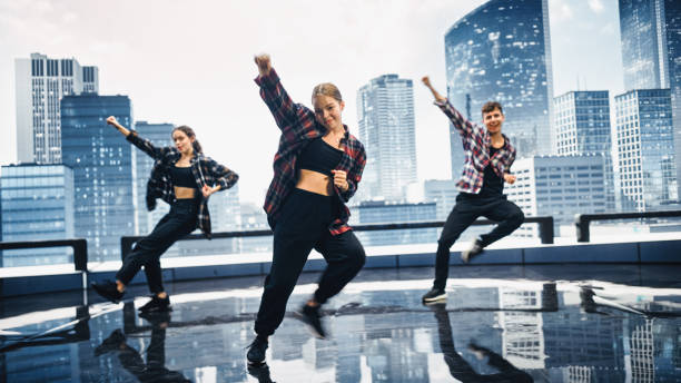 istock Diverse Group of Three Professional Dancers Performing a Hip Hop Dance Routine in Front of a Big Digital Led Wall Screen with Modern City Skyline with Office Skyscrapers in Studio Environment. 1388326575