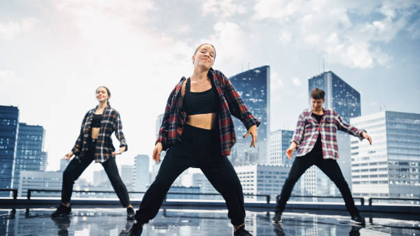 istock Diverse Group of Three Professional Dancers Performing a Hip Hop Dance Routine in Front of a Big Digital Led Wall Screen with Modern Urban Skyline with Office Skyscrapers in Studio Environment. 1388326604
