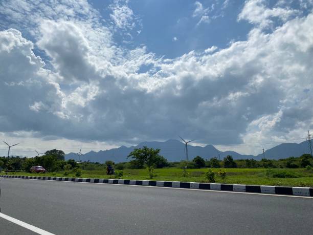 istock Wind power station, windmill with storm cloudy sky and road background 1388331846