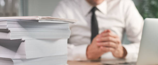 To much paperwork, businessman at the desk with piled business paper to be archived stock photo