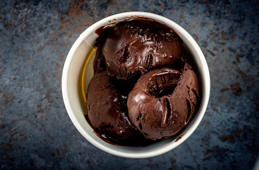 Chocolate ice cream balls in a white paper Cup on a gray stone background
