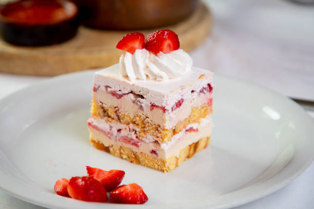 Cube slice of sponge cake layered with cream and strawberries in a plate, dessert served on restaurant table