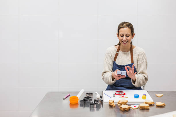 istock Pastry chef using her phone while decorating cookies in pastry shop 1388336125