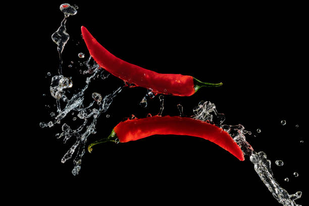 istock Two red hot peppers in water splash over black background 1388336407