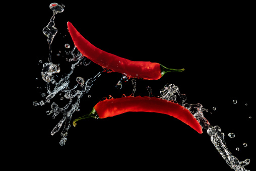 Two red hot peppers in water splash over black background