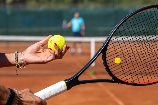 Close-up of hands holding racket and tennis ball on clay court.