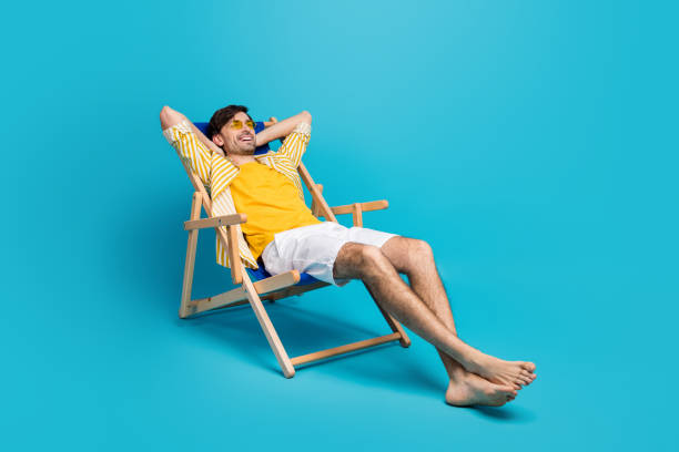 foto laterale del profilo a figura intera del viaggiatore positivo relax riposo spiaggia sole sdraio sdraio sdraio allungare le mani indossare pantaloncini bianchi isolati su sfondo di colore blu - sedia a sdraio foto e immagini stock