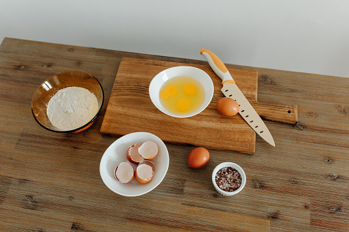 Cooking in progress. Eggs, flour, salt on the table, cutting board and knife. Dough Ingredients. View from above