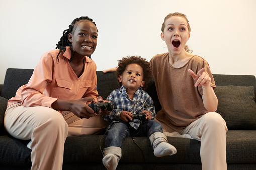 Happy mothers and little son playing video game together at home