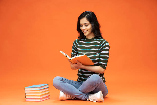Young woman sitting on floor with book on orange background, stock photo stock photo