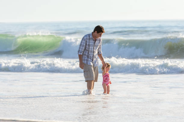 istock Father and his two young daughters playing with the ocean waves on the beach 1388345414