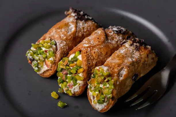 Photo of Close up of Cannoli Siciliani - traditional italian dessert stuffed with ricotta cheese cream and decorated with pistachios and chocolate.