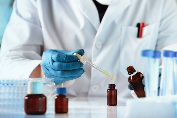 mãos de tubulação química em uma gota de garrafa de perfume fluido amarelo no laboratório de pesquisa de produtos - preparação magistral - fotografias e filmes do acervo