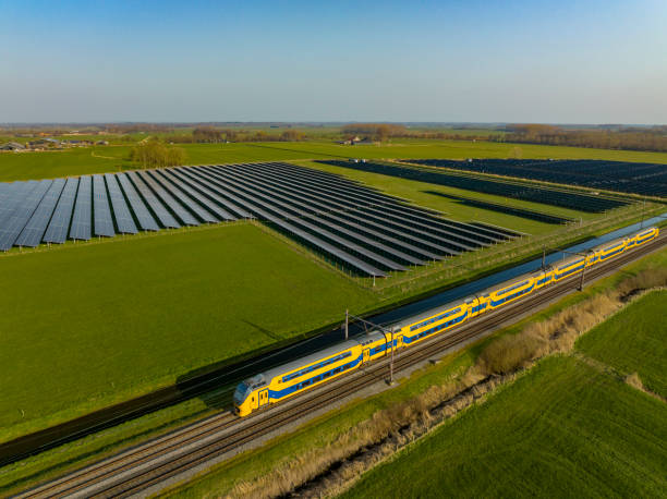train of the dutch railways driving past a field of solar panels seen from above - trein nederland stockfoto's en -beelden