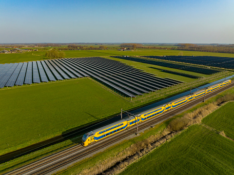 Train of the Dutch Railways driving past a field of solar panels seen from above