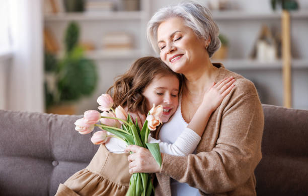 おばあちゃんに花や贈り物をする優しい女の子 - grandmother senior adult smiling women ストックフォトと画像