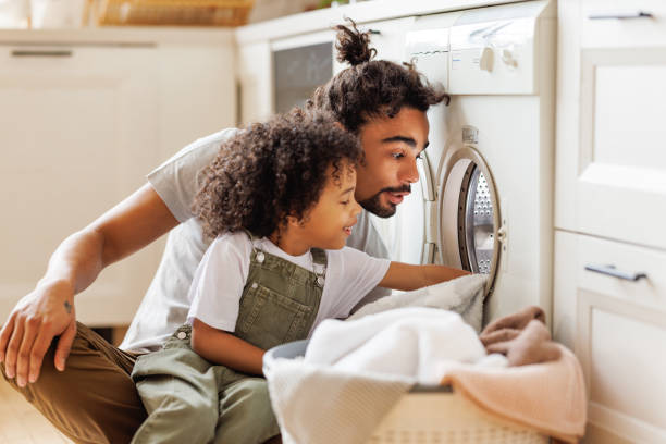 sohn hilft papa, waschmaschine zu beladen - washing stock-fotos und bilder