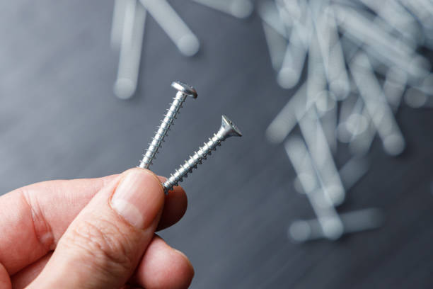 hand holding two steel screws on a black and white background - screw human head bolt isolated imagens e fotografias de stock