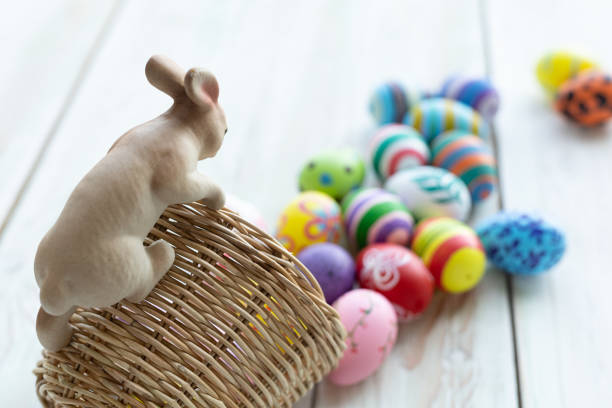 concepto de vacaciones de pascua, adornos de jardín estatuas de conejo en canasta con coloridos huevos de pascua en color pastel blanco fondo de madera rústica con espacio. - animal egg eggs basket yellow fotografías e imágenes de stock