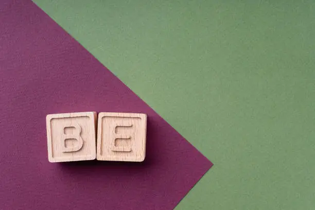 Photo of BE is a word made up of wooden cubes on a scarlet and green background. The phrase calls for action, the slogan. A bright creative concept. Be who you want to be