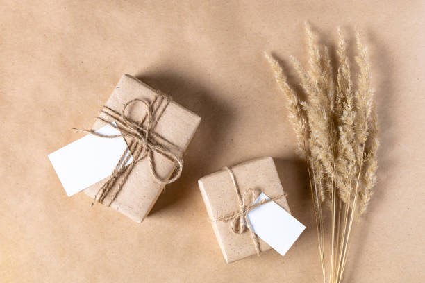 empty white gift tag mock up on craft paper box with dried spikelets decoration on natural beige background.