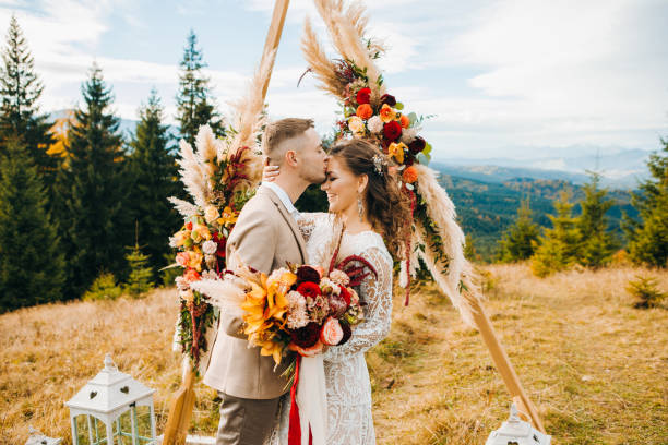cérémonie de luxe dans les montagnes avec une vue imprenable. le marié embrasse sa femme sur le front - cérémonie photos et images de collection