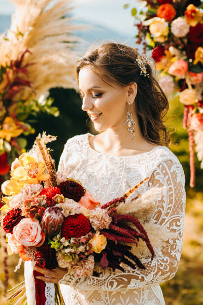 mariée heureuse en robe blanche élégante, avec un bouquet de mariage, un magnifique paysage de montagnes en arrière-plan.  maquillage naturel, coiffure - young men young women bride hairstyle photos et images de collection