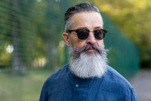 Suave and Sophisticated A portrait of a mature man wearing sunglasses, standing outdoors in Newcastle upon Tyne, England. He is looking to his side with a serious look on his face. slicked back hair stock pictures, royalty-free photos & images