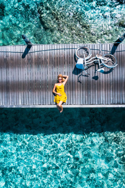 Beautiful woman lying down on jetty with bicycle in Maldives Beautiful woman lying down on jetty with bicycle in Maldives jetty aerial stock pictures, royalty-free photos & images