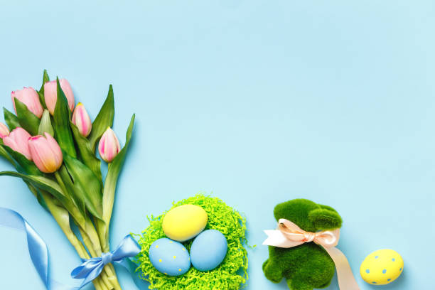 istock Easter composition tulips spring flowers eggs in a nest toy rabbit on a blue background. 1388366364