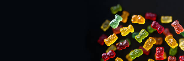 istock Multicolored flying gummy bears on a black background, flat lay. Banner 1388366392