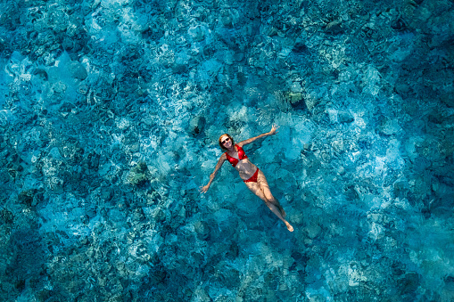 Woman lying on crystal water over reef in ocean