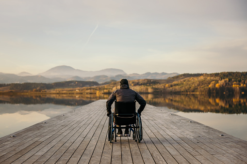 Paraplegic handicapped man in wheelchair admiring lake and mountain from wooden pier