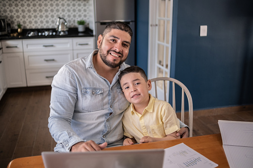 Portrait of Latin boy studying and father working at home