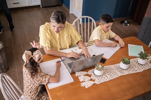 Latin mother working and helping daughter with homework at home