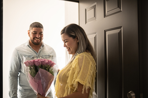 Latin mid adult man giving flowers to wife at home