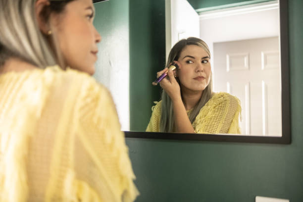 Latin woman applying make up looking in the mirror in the bathroom stock photo