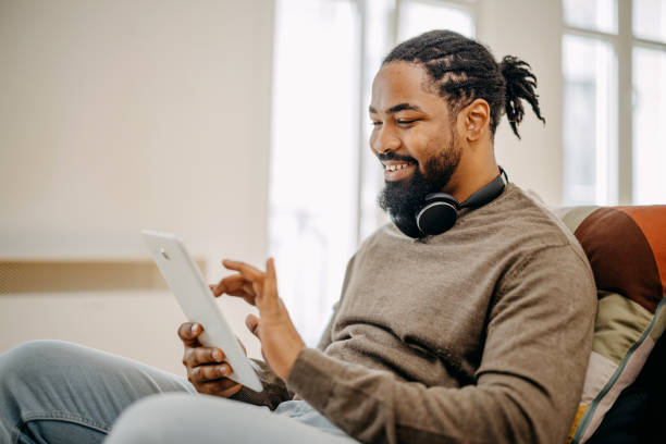 istock Relaxed black man using digital tablet and smiling while sitting on the sofa at home 1388373466