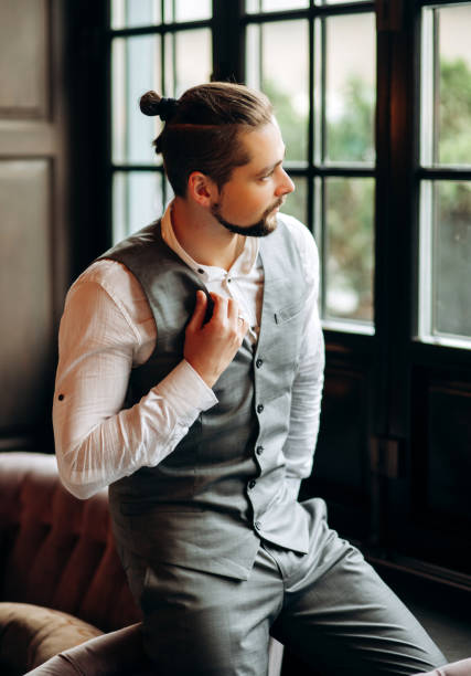 Stylish man with a beard in a graceful suit looks out the window.