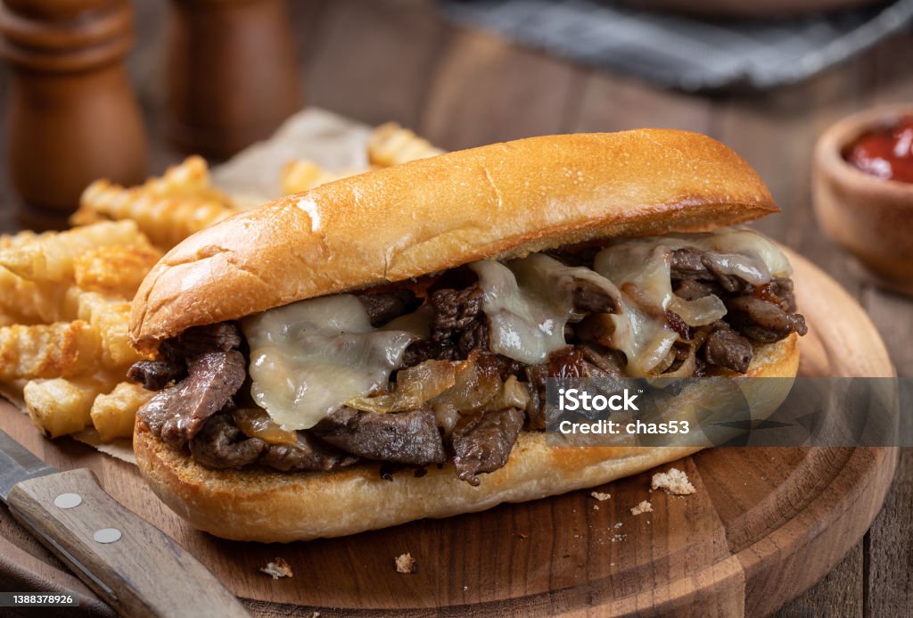 Philly cheesesteak sandwich and french fries Philly cheesesteak sandwich made with steak, cheese and onions on a toasted hoagie roll with french fries on a wooden board Philadelphia Cheese Steak Stock Photo