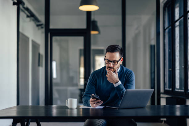 istock Serious male, reading something from his mobile phone, holding a hand on his chin. 1388379747