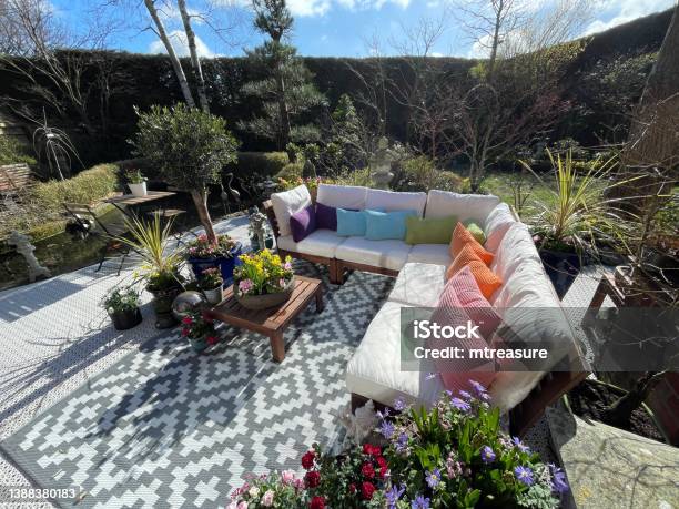 Image Of Outdoor Lounging Area In Spring Hardwood Seating With Cushions Wooden Table Top With Flowering Plant Centrepiece Bonsai Trees Japanese Maples Koi Pond Landscaped Oriental Design Garden Sunny Day Focus On Foreground Stock Photo - Download Image Now