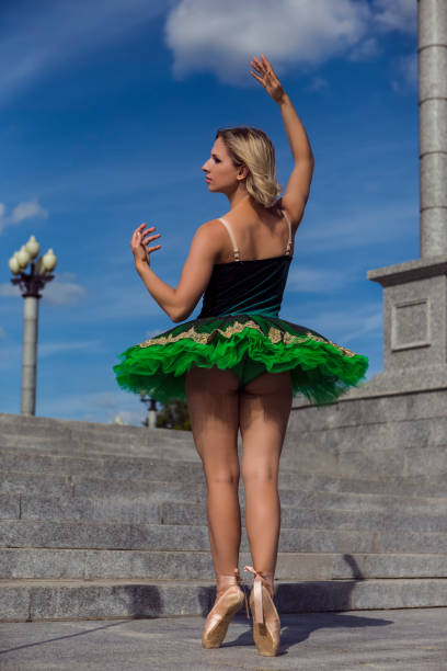 istock Ballet Dance Ideas. Tranquil Calm Winsome Elegant Professional Caucasian Ballet Dancer in Green Tutu Dress Posing in Dance On Stairs With Lifted Hands Pose Outdoor 1388381547