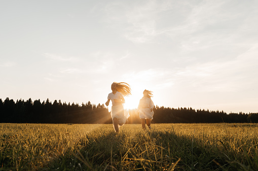 Mother and daughter run in field, sunset light. Copy space.