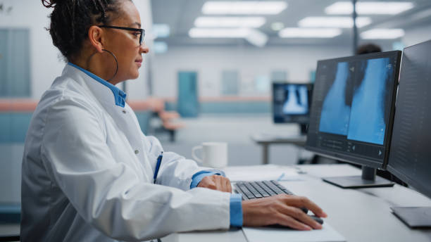 istock Hospital Laboratory: Black Female Medical Doctor is Working on Computer Analysing Chest, Bones X-rays on Screen. Professional African American Physician Doing Health Care Treatment Research 1388386363