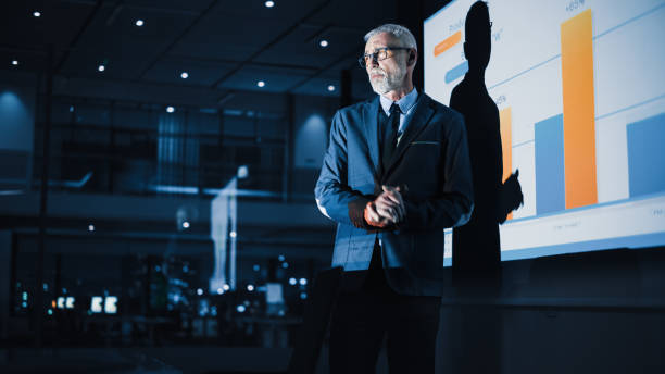 istock Conference Business Meeting Presentation: Chief Executive Officer Shows Data to Diverse Group of Investors, Businessspeople. Projector Screen Shows Graphs, Product Sales Growth, e-Commerce Analysis 1388387603