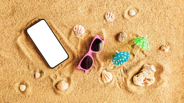 istock Smartphone with blank screen on the beach. Summer holiday (vacation) - background banner. 1388387693