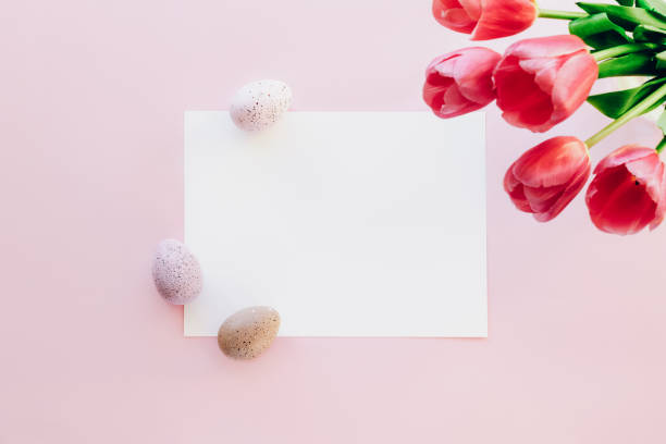 istock Blank white sheet and red tulips, decorated Easter eggs on pink background. Easter concept. Top view, flat lay, mock up 1388387807